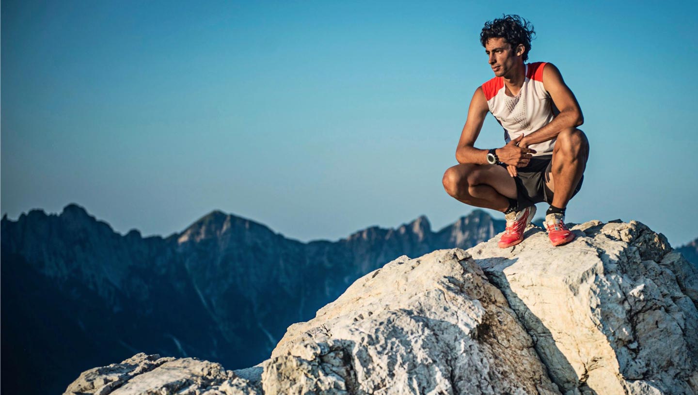 Coureur de montagne en tenue de sport accroupi sur un rocher