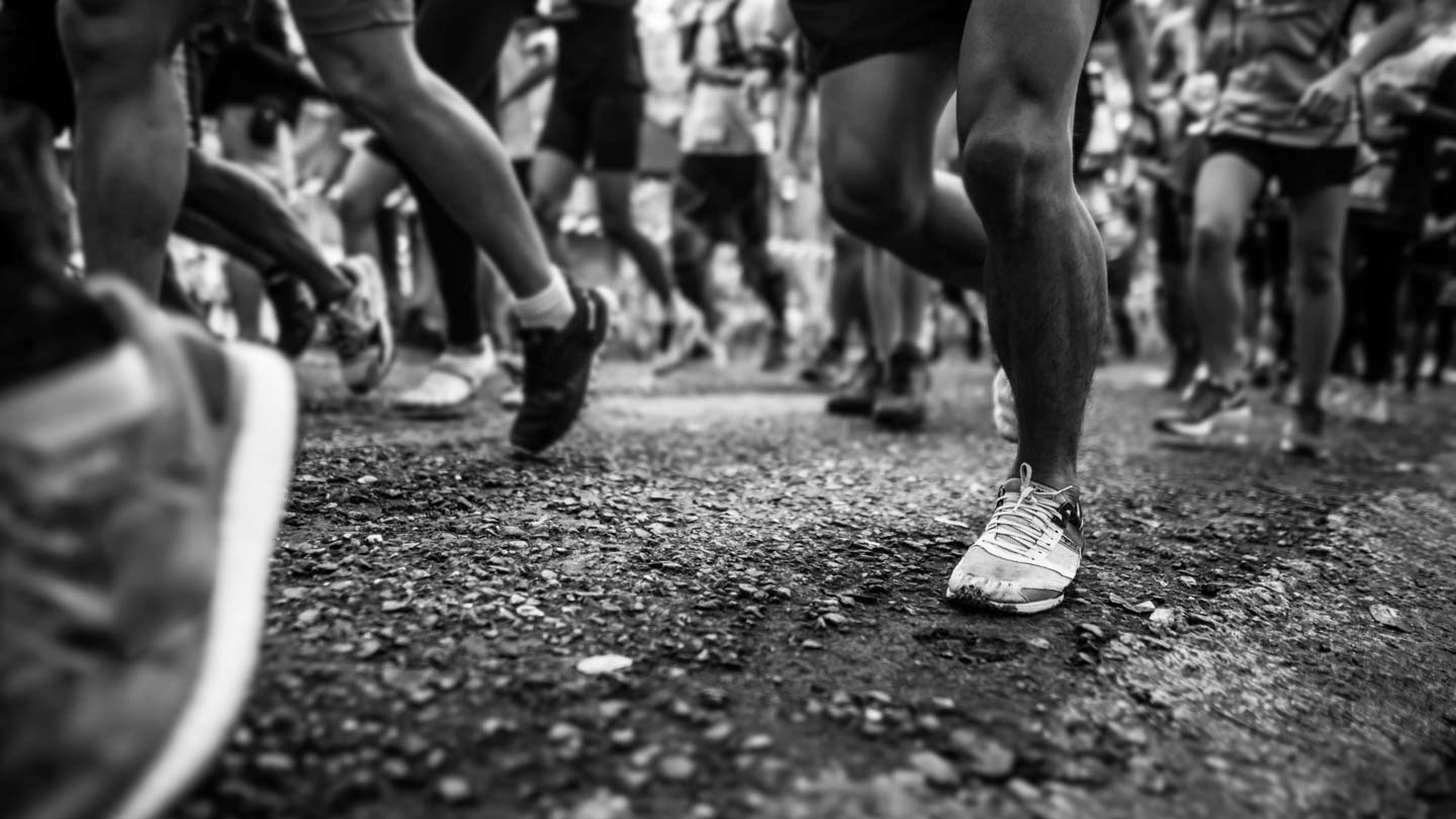 photo en noir et blanc des pieds de coureurs d'un marathon sur une route goudronnée